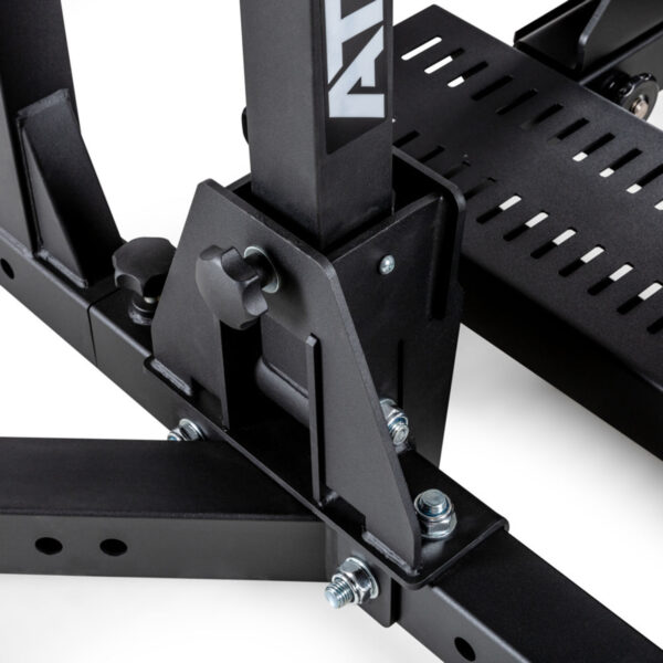 Close-up of a black metal bracket with bolts, part of the ATX® Competition Combo Rack. The bracket has an adjustable knob and is attached to a base with slotted details, showcasing industrial design elements.

.