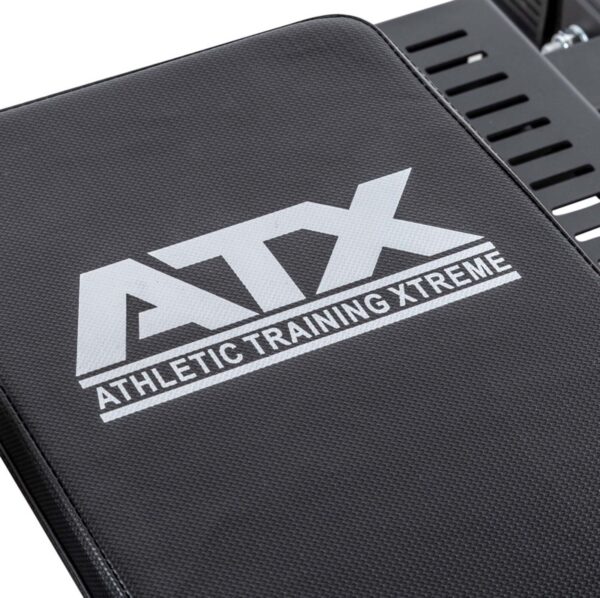 Close-up of a black exercise bench with the ATX® Competition Combo Rack logo in white, with parts of the metal support structure visible in the background.