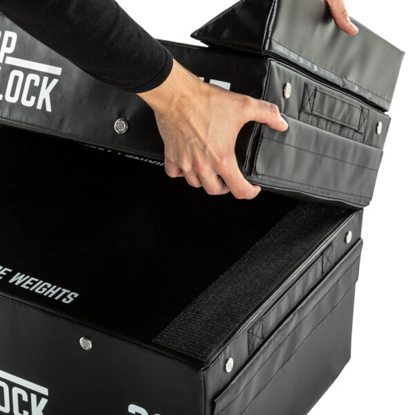 A person stacks ATX® 15 cm Soft Drop Blocks, featuring black padding with Velcro fasteners and branded text.
