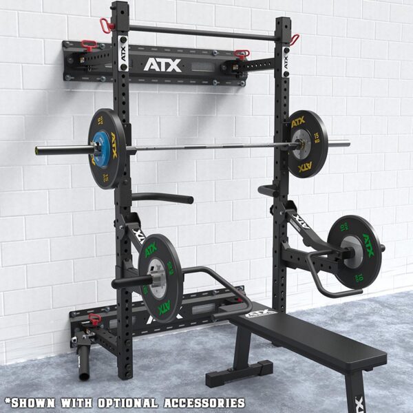A folding wall-mounted squat rack with a weightlifting barbell and plates is shown. A bench is positioned nearby for versatile workouts. The setup, featuring ATX branding, stands against a white brick wall. Optional accessories are included.