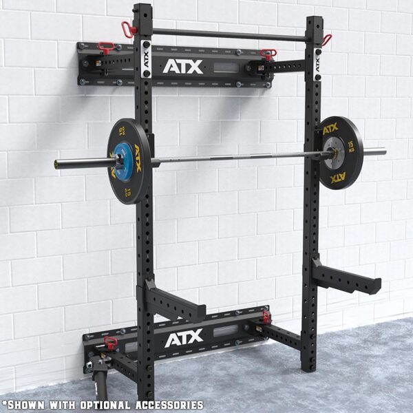 A black ATX® Fold Back Rack Mount Rails is attached to a white brick wall, supporting a barbell with weight plates. The floor is cement, and the image mentions optional accessories.
