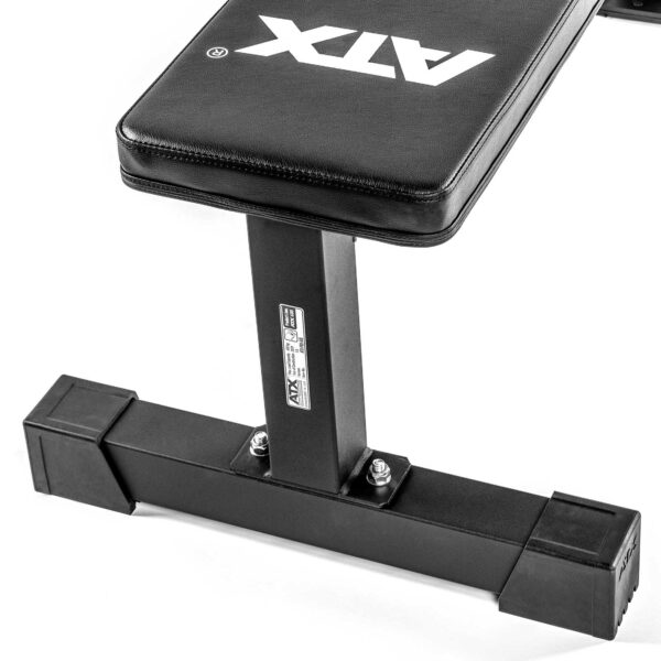 Close-up of the leg support on a black ATX® Flat Bench PRO, featuring a padded seat and sturdy metal frame. The bench includes visible screws and rubber feet for stability during workouts.