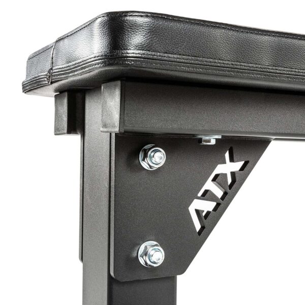 A close-up reveals the ATX® Flat Bench, showcasing its sturdy black frame and cushioned seat. Metal bolts secure the structure, and a cut-out ATX logo graces the side support, emphasizing durability and strength for heavy-duty workouts.