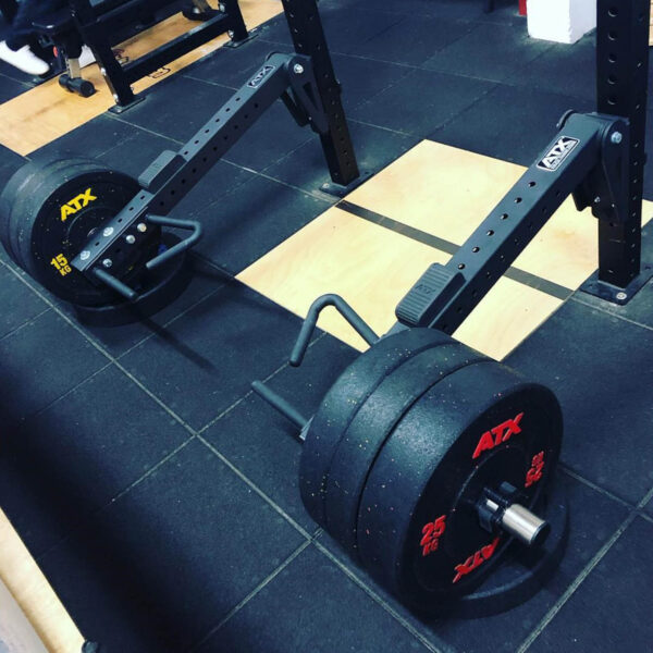 A loaded ATX® Jammer Arms bar with multiple weight plates rests on a gym floor. The plates display red and yellow lettering for the weights, and the setup is in a gyms lifting area.