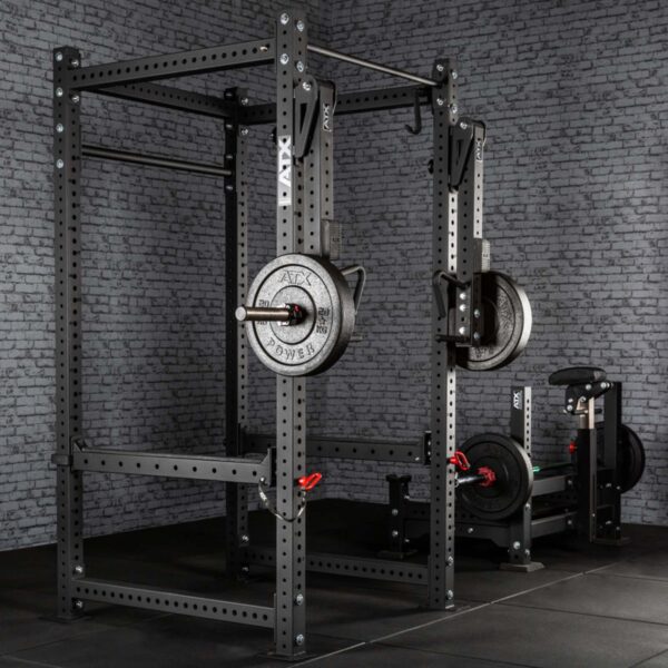 A gym featuring ATX® Jammer Arms attached to a power rack holds a barbell with weight plates against a textured gray brick wall. The floor is covered in black mats, and an incline bench press with extra weights is visible in the background.