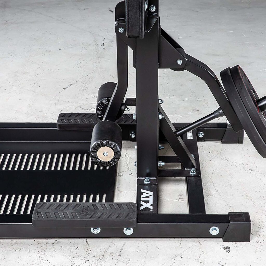 Close-up of a black leg press machine, similar to the robust ATX® Leg Master, with metal plates and padded rollers on a gray concrete floor. Labeled ATX.