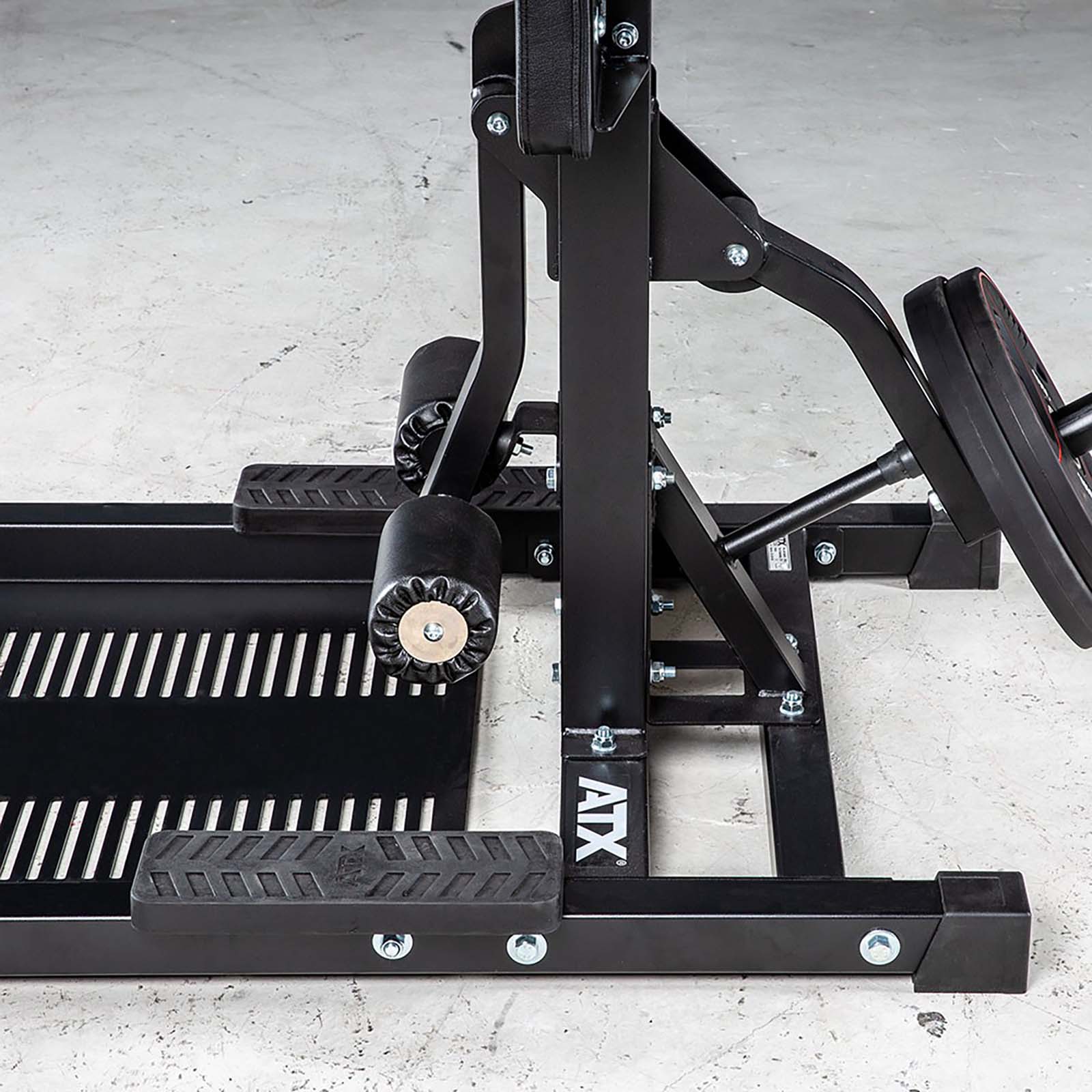 Close-up of a black leg press machine, similar to the robust ATX® Leg Master, with metal plates and padded rollers on a gray concrete floor. Labeled ATX.