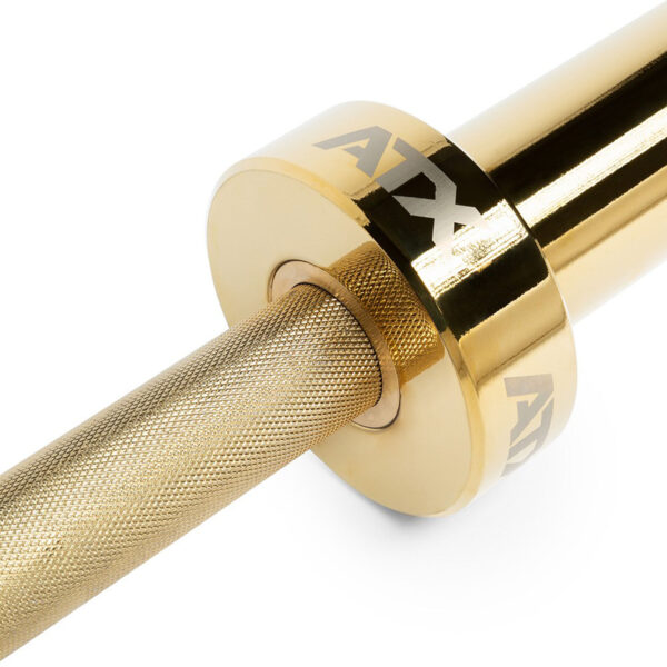 A close-up of the ATX® Olympic Golden Powerlifting Bar reveals its gold-colored, textured grip and shiny cylindrical end engraved with ATX, which reflects light to highlight its metallic finish.
