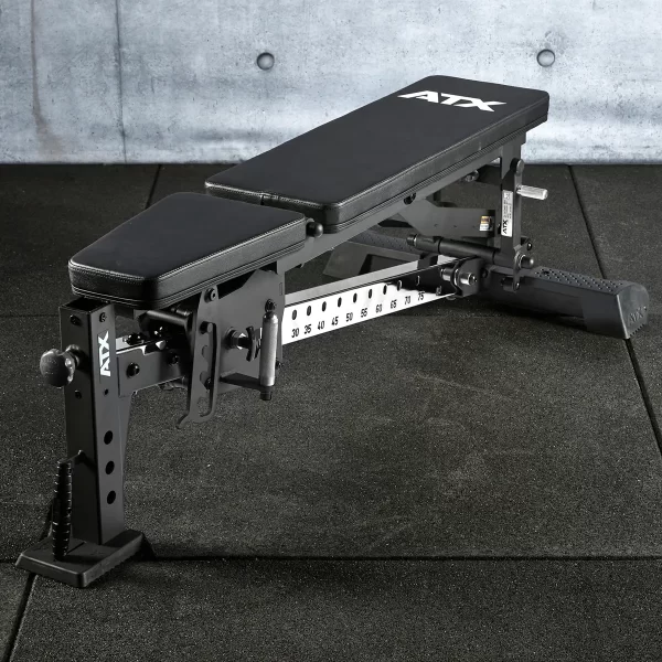 The ATX® Multi Bench features a padded seat and backrest on a textured dark surface with branding. It includes an inclination number scale for adjustments and is set against a concrete wall backdrop.
