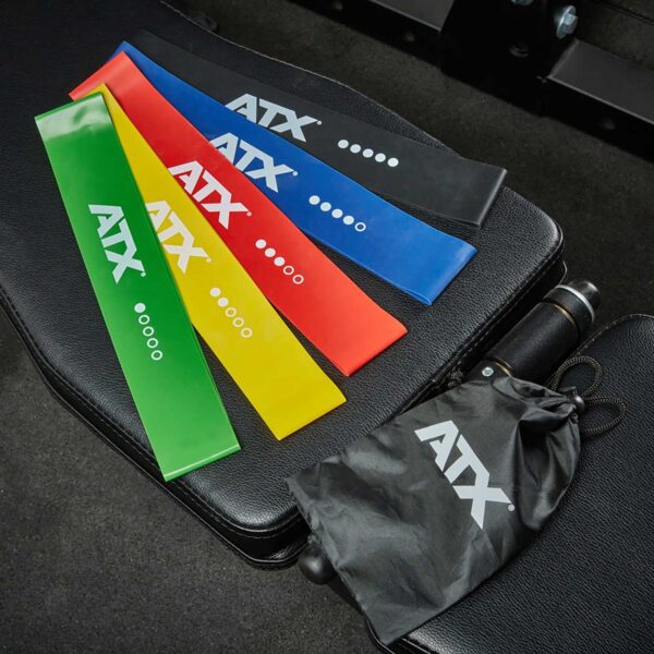 The ATX® Mini Band Set, featuring assorted colored bands (green, red, yellow, blue, black), is displayed on a black surface with a black drawstring bag and a cylindrical object nearby.
