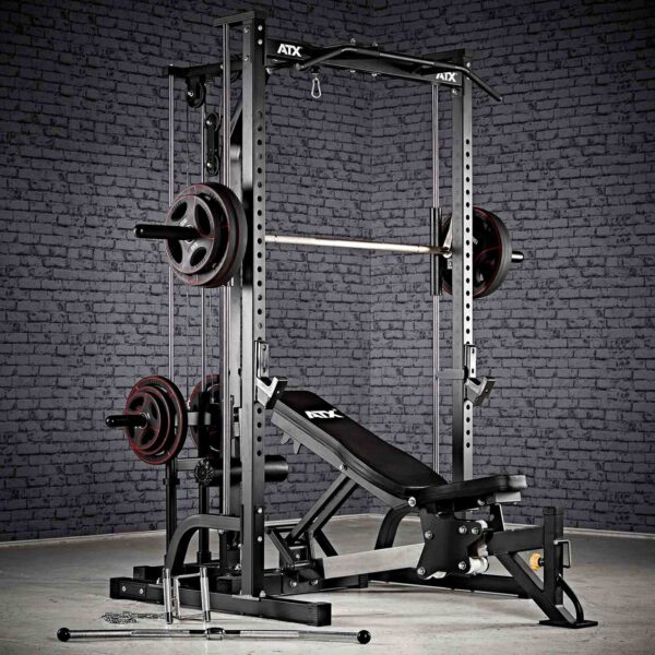 A home gym setup showcasing the ATX® Smith Machine System Plate Loaded, accompanied by a barbell, weight plates, and an adjustable bench, all set against a brick wall backdrop.