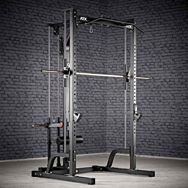 A black ATX® Smith Machine System Plate Loaded is set on a gray floor against a dark brick wall, featuring a pull-up bar, adjustable safety bars, and weight storage pegs.