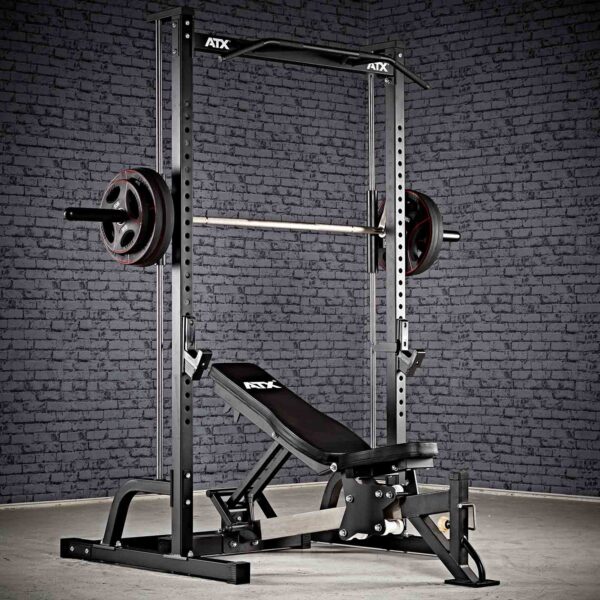 The ATX® Smith Machine Half Rack, featuring a barbell and weight plates, paired with an adjustable bench, sits against a textured gray brick wall on a concrete floor.