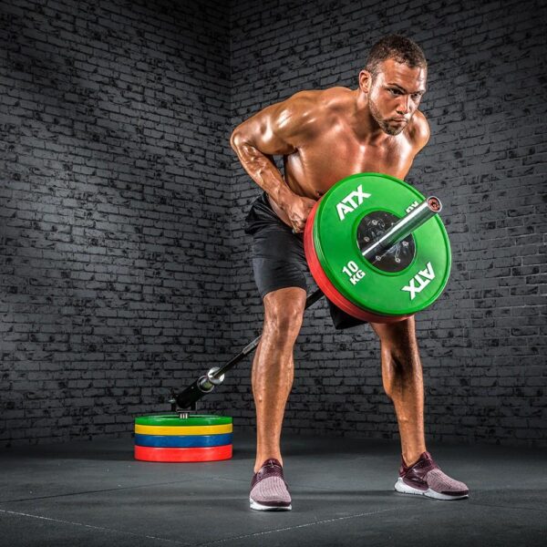 A muscular man executes a bent-over row with a 7ft 1500lbs Olympic Bushing Bar using green and red weight plates, skillfully wielding an ATX Parallel Grip T Bar Row Handle in a gym with a gray brick wall and stacked weights nearby.