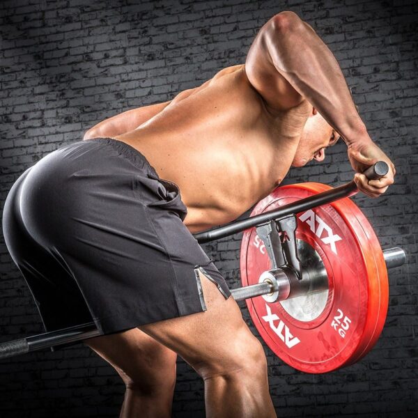 A muscular person performs a rowing exercise shirtless in black shorts against a dark brick wall, lifting a Power Maxx 4ft Olympic Barbell with red weight plates using an ATX Wide Grip T Bar Row Handle.