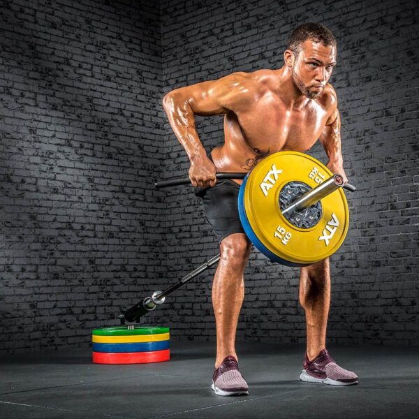 A muscular man, shirtless in black shorts and maroon shoes, does a bent-over row with a Power Maxx 4ft Olympic Barbell loaded with colored weight plates. Standing in a room with gray brick walls, the equipment contrasts against the dark space.