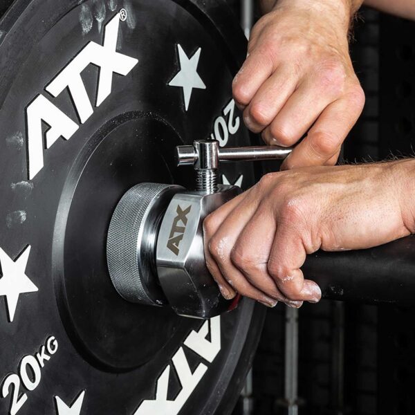 Close-up of hands using a tool to tighten an ATX® Competition Collars Short IPF onto a 20 kg weight plate marked ATX in a gym, ensuring the weight is secure for lifting.