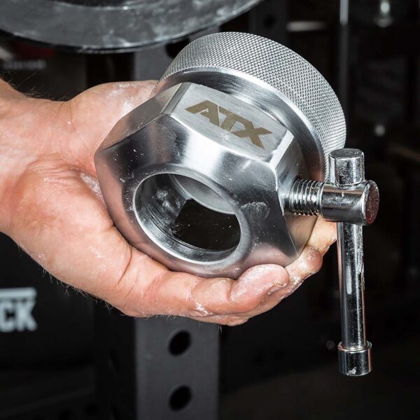 A hand holds the ATX® Competition Collars Short IPF, featuring a metallic body with a knurled grip and adjustable screw, ATX engraved, set against gym equipment.