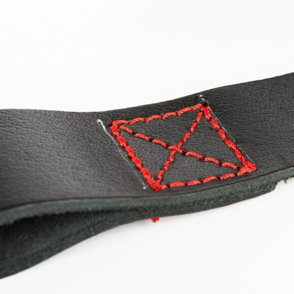 The ATX® Bulls Strongman Yoke features a close-up of its black leather strap with striking red stitching in a square-X pattern, reminiscent of robust strongman gear. The detailed stitching contrasts beautifully against the smooth leather, all set on a plain white background.