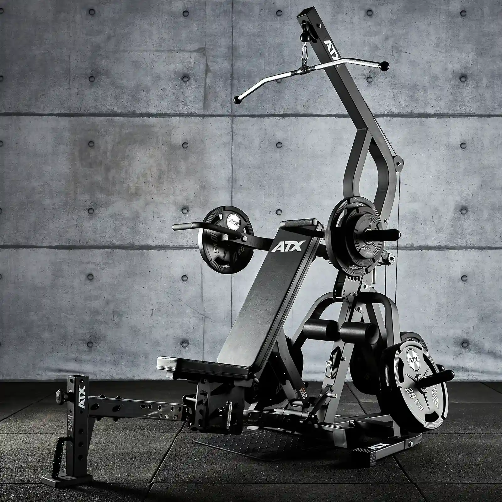 The sleek and black ATX® Triplex Multi Gym features a multifunctional design, including a weight bench, various weights, and a pull-down bar. Ideal for strength training enthusiasts, it complements any modern grey concrete wall as a compact home gym setup.