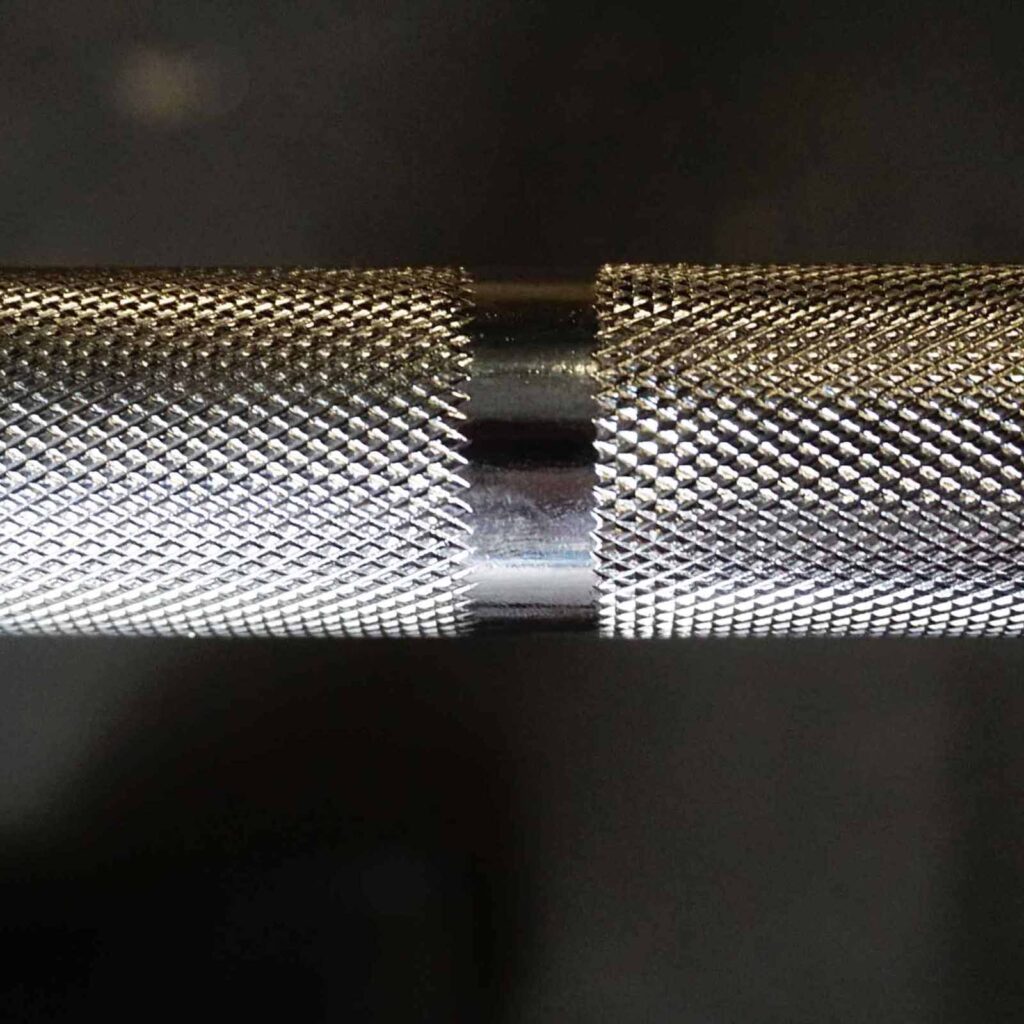 Close-up of a 7ft Olympic Barbell 1000lbs against a dark background, highlighting its textured, knurled grip with an intricate pattern that provides a superior rough surface for enhanced grip.