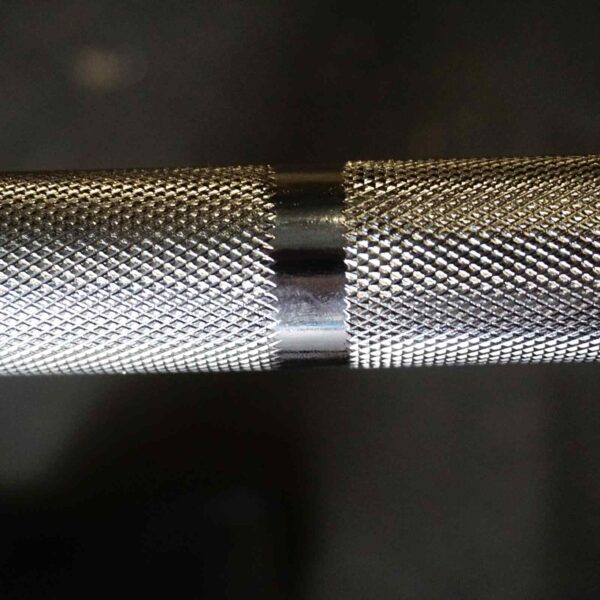 Close-up of the 7ft 1500lbs Olympic Bushing Bar with a diamond-patterned grip. Its smooth, polished center reflects light against a dark, blurred background, enhancing the barbells intricate details.
