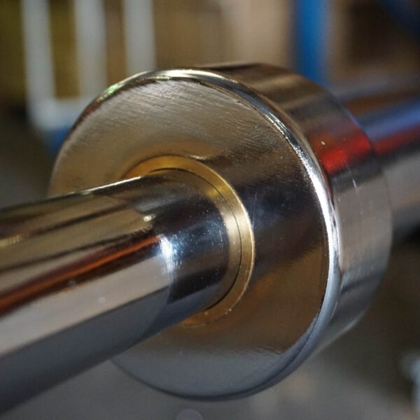 A close-up of the 7ft 1500lbs Olympic Bushing Bar highlights its polished finish, with detailed focus on the end cap and sleeve. A slightly blurred background accentuates the bars reflective surface.