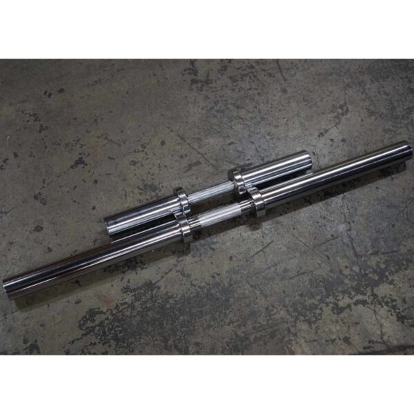 Two Power Maxx Big Olympic Dumbbell Handles lie parallel on a textured concrete floor, their metallic surfaces glinting in the light and featuring smooth, cylindrical sections ready for weights.