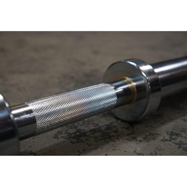 Close-up of a Power Maxx Big Olympic Dumbbell Handle, featuring a textured silver grip and smooth weight collars, resting on a rough floor.