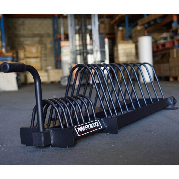 In a warehouse, a Bumper Weight Plate Toaster Rack sits on the concrete floor. Its black metal frame, akin to a sturdy toaster rack, offers slots for organizing weight plates against shelves and boxes.