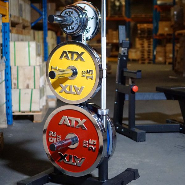 A rack holds colorful yellow, red, and silver ATX weightlifting plates in a gym. The scene features a Power Maxx Olympic Weight Plate Stand with fitness equipment and a bench in the background.