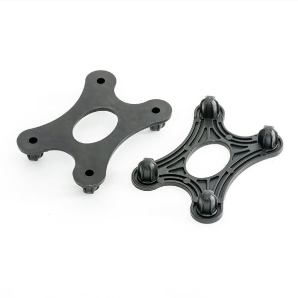 Two black, four-pronged GymFloor® RTS Turf components with oval centers are shown. One is solid with a smooth surface; the other has a grooved design and knobs at each tip. Both sit on a white background.