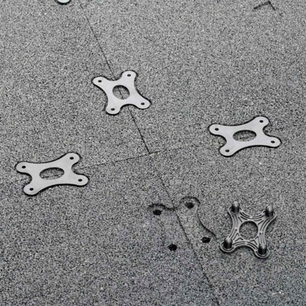 Close-up of GymFloor® RTS Turf 50x50@20mm textured surface with scattered metal brackets featuring a four-hole design. A small indentation is visible near the center.