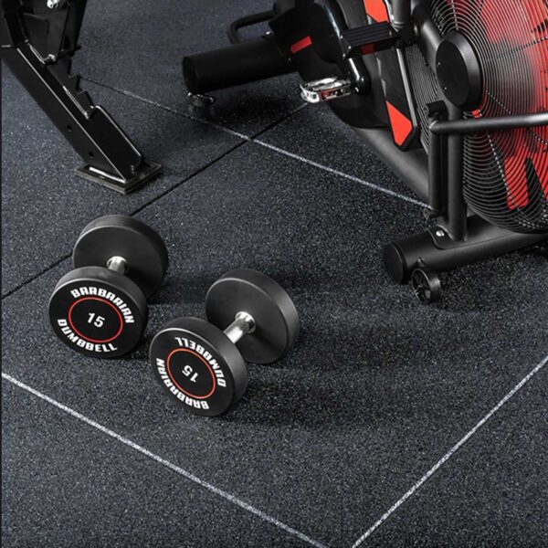 Two black dumbbells labeled 15 lie on a GymFloor® 15mm 1m x 1m Black surface, beside a stationary exercise bike in a workout area.
