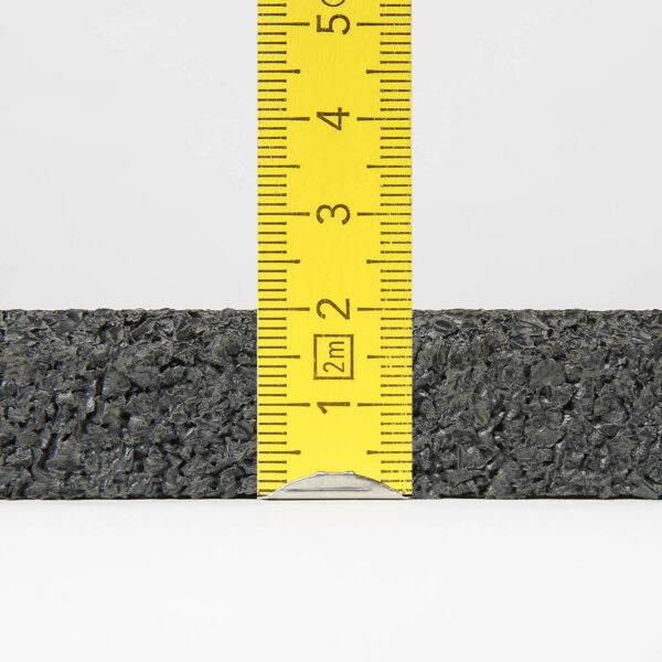 A close-up image of a yellow ruler standing vertically against the textured black surface of a Gymfloor® 20mm 1m x 1m mat, with the rulers measurements showing the black material is approximately 2.5 inches (6.5 centimeters) tall.