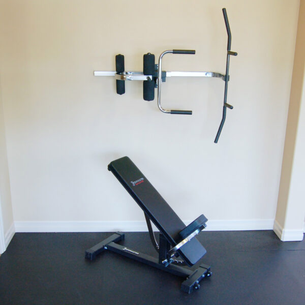 A minimalist home gym setup features the Ironmaster Ultimate Chin Up Attachment for the IM2000 and an adjustable weight bench below, complemented by neutral-colored walls and a dark floor mat.