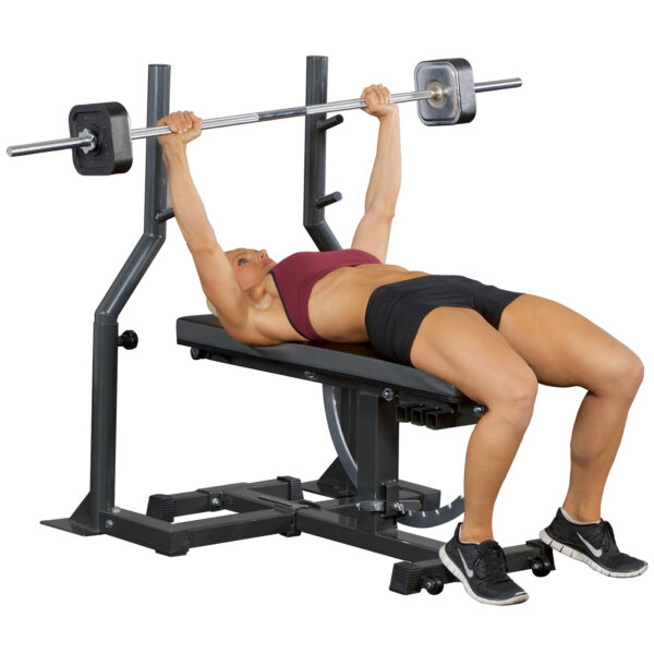 Dressed in athletic gear, an individual uses the Ironmaster Barbell Attachment on a bench to press weights. The gym setup features a robust support frame and organized weight racks, while the individuals focused expression shows their effort.