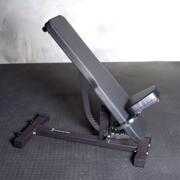 The Ironmaster Hybrid Bench Pad, a black adjustable weight bench with a comfortable padded seat and backrest, is inclined and stable on a textured dark gym floor.