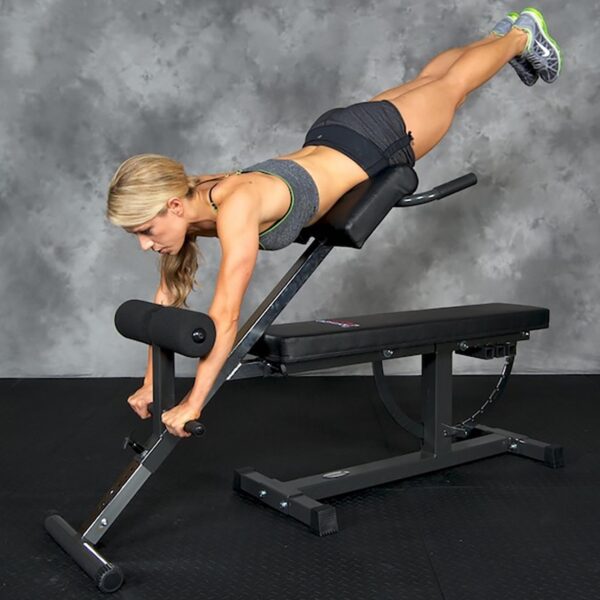 Using the Ironmaster Hyper Core Attachment, a person in athletic clothes performs an exercise, leaning forward with straight legs. The backdrop is a grey textured wall.