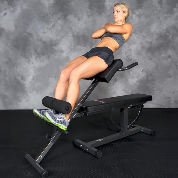 An individual in athletic wear uses the Ironmaster Hyper Core Attachment for a back extension exercise in a gym, with a textured gray wall and dark gym flooring in the background.