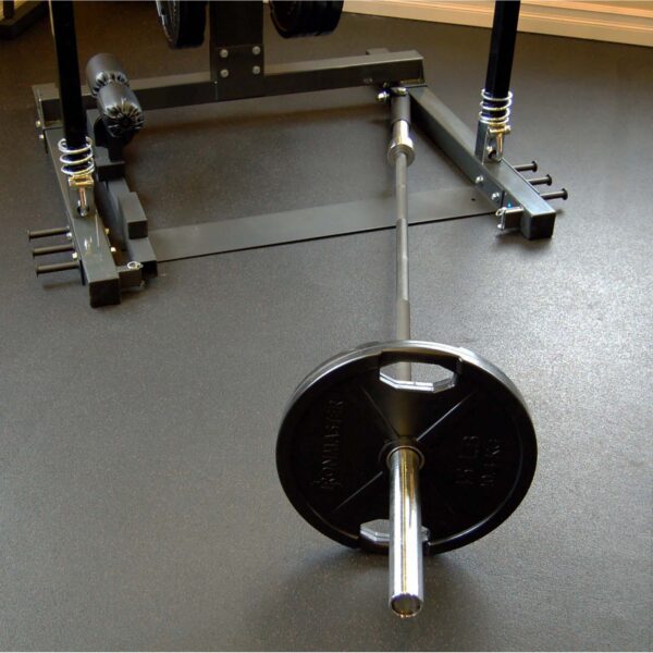 An Ironmaster Landmine Attachment, accompanied by a barbell and weight plates marked 45 lbs, rests on a gyms dark rubberized floor in front of a squat rack, indicating a designated weightlifting area.