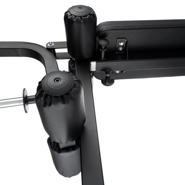 Close-up of the Ironmaster Leg Lift PRO, highlighting its padded rollers and bench. The focus is on the padding and robust metal frame that emphasize its construction and design features.