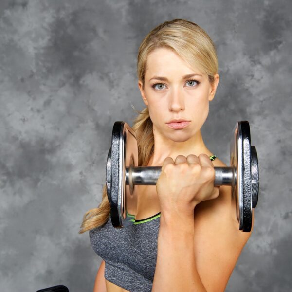 A person with long hair exercises using Ironmaster 45lb Adjustable Dumbbells. Theyre wearing a gray sports top, looking focused, against a textured gray background.