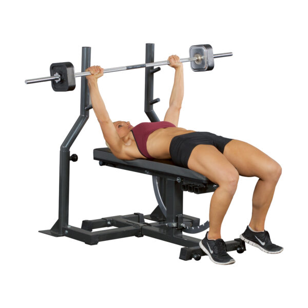 A person in athletic attire lies on a weightlifting bench, feet flat, as they perform a bench press with the Ironmaster Straight Barbell, pushing it upwards.