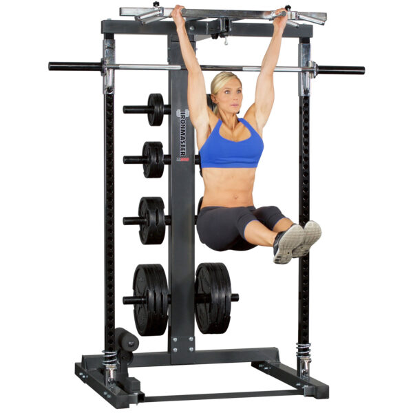 A woman in athletic clothing performs a hanging leg raise using the Ironmaster Ultimate Chin Up Attachment for IM2000, showcasing her strength and balance in the gym. Weights are stacked on the sides for added resistance.