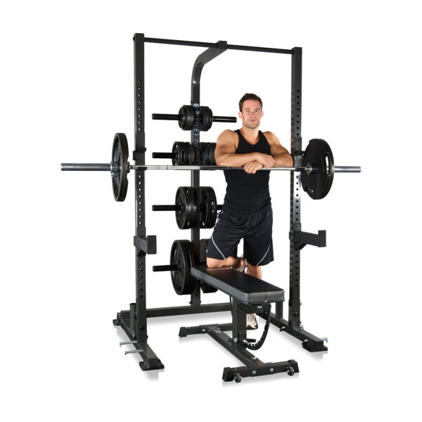 A person in athletic attire is kneeling on a weight bench, leaning on an IM1500 Ironmaster Half Rack loaded with weights in a gym setting, suggesting strength training.