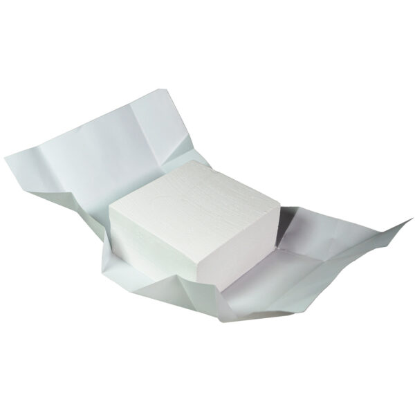 A white block of butter paper sits partially unwrapped on a flat surface, resembling a chalk box. The paper is creased and unfolds around the rectangular block, showcasing the texture and thickness. The plain white background completes the minimalist scene.