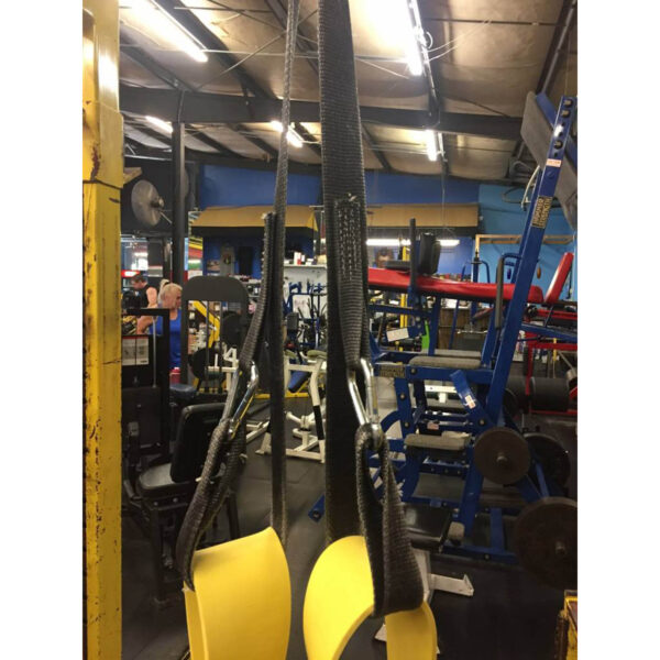 A close-up of the Spud Inc The Big Ray Strap, featuring yellow hanging ab straps suspended from black straps, is set against a backdrop of weightlifting machines, benches, and gym accessories in a bustling fitness facility.