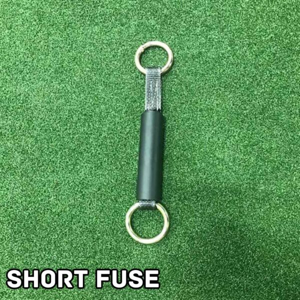A dynamite stick labeled Spud Inc Dynamite Stick Short/Long Fuse features a short fuse with two metal rings at each end, resting on a grassy green surface. The words SHORT FUSE appear boldly in white at the bottom left corner.