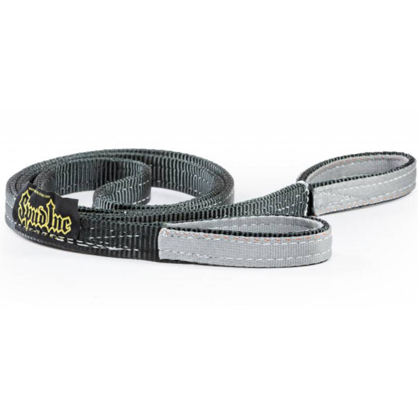The Spud Upper Body Sled Strap, black and gray with a woven texture, is coiled against a white background. Near one end, it displays a small rectangular logo tag in yellow and black.